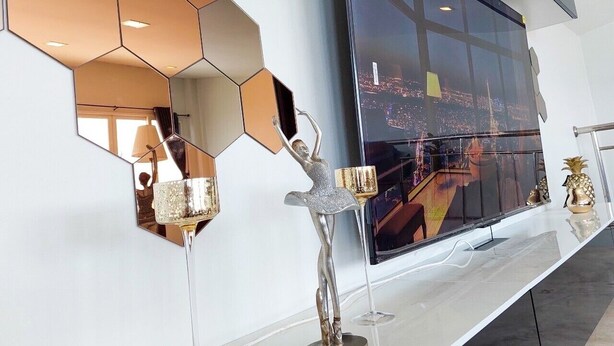 Un interior moderno con un televisor de pantalla plana grande, decoración mural hexagonal y una escultura plateada decorativa.