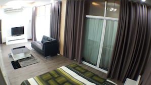 A modern hotel room with a sofa, a TV, a large window with curtains, and a bed. - Maximum Luxury Apartment (Udon Thani)