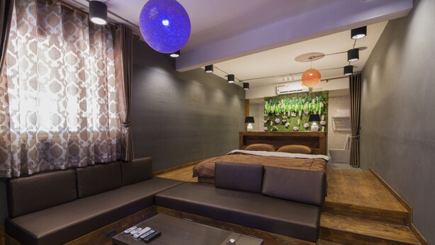 A modern bedroom with a large bed, a built-in bench, a coffee table, and a wall-mounted air conditioning unit. - Maximum Luxury Apartment (Udon Thani)