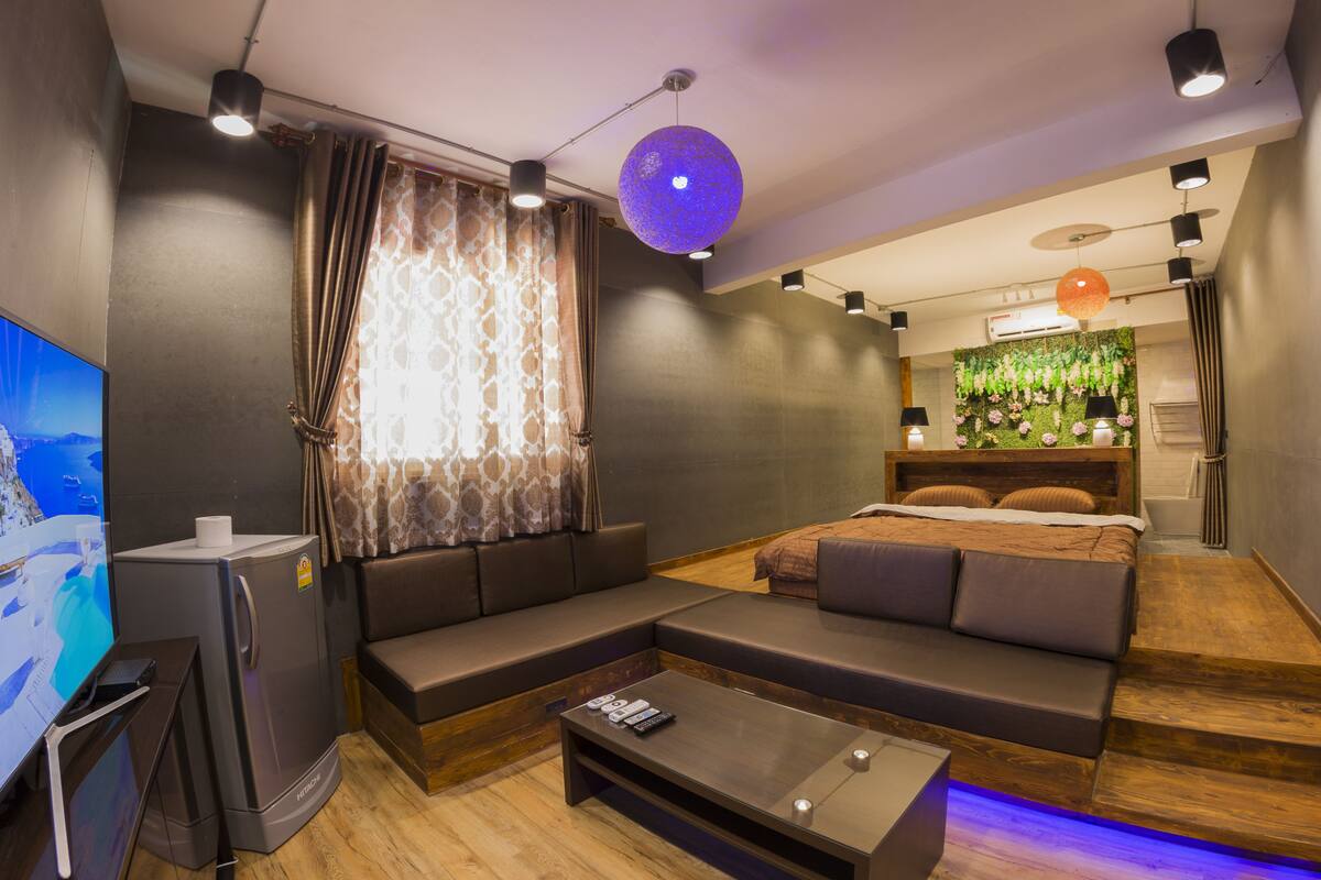 Una habitación de hotel moderna con un sofá modular, un televisor de pantalla plana, un refrigerador compacto y una pequeña mesa de centro de madera.