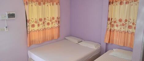 A room with two beds, a wall-mounted heater, and a window with curtains.