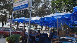 Un puesto a la vera de la carretera con sombrillas azules, un letrero que dice "Pana Resort" y un coche rojo estacionado cerca.