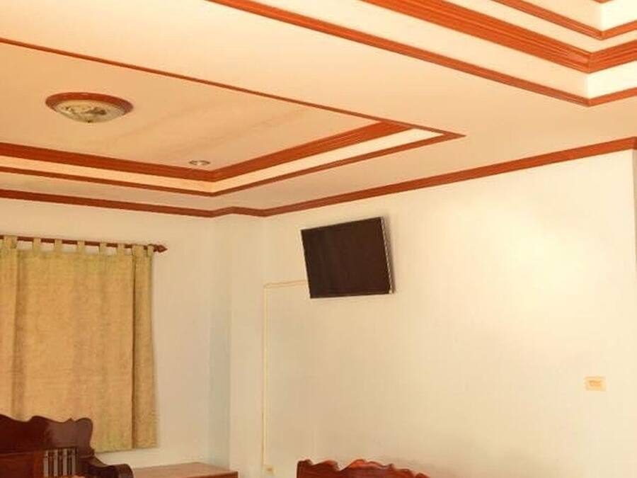 Una habitación con un sofá de madera, una mesa y un televisor montado en la pared.