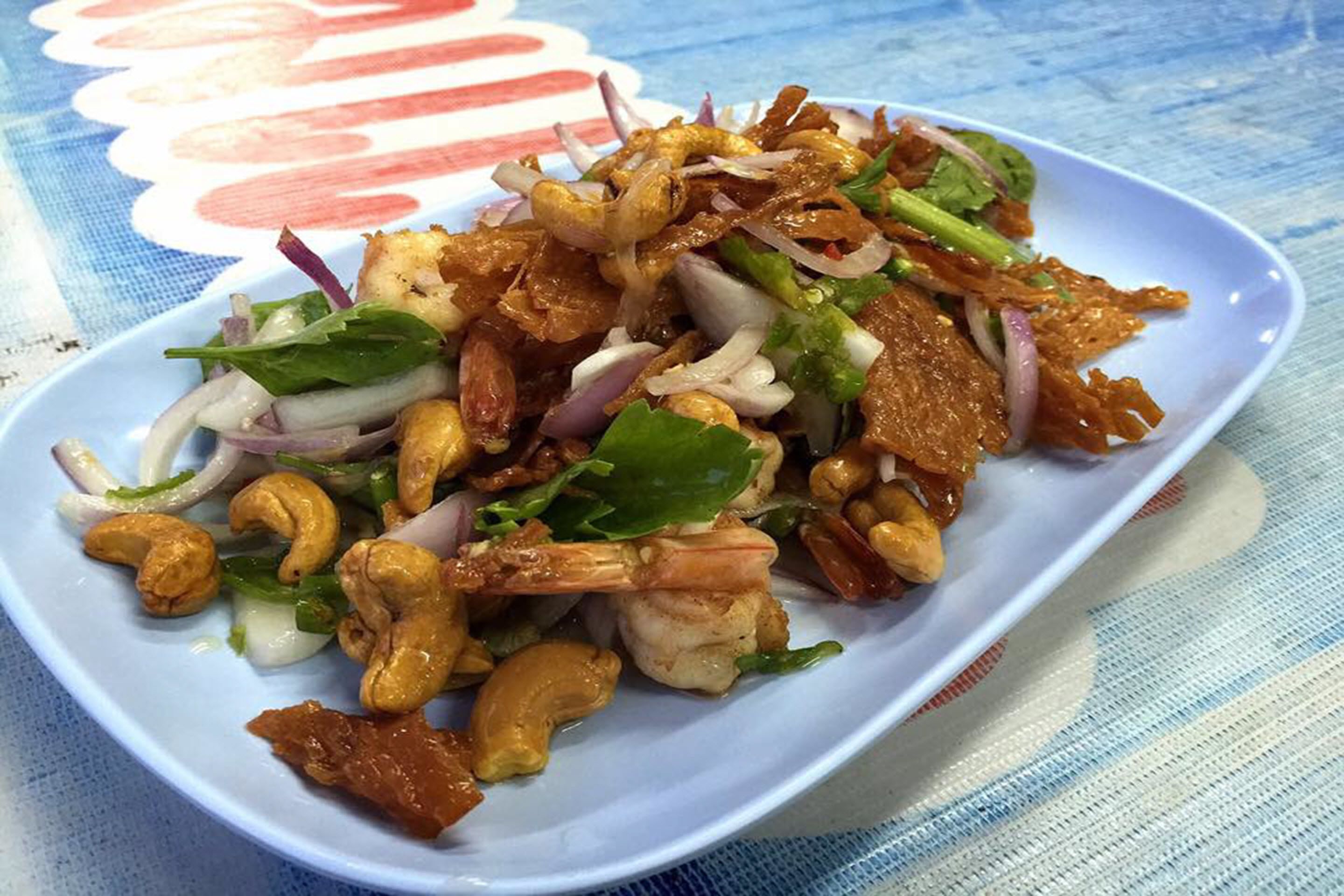 Un plato de comida con camarones, nueces de cajú y verduras.