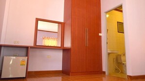 Habitación con un armario de madera, un refrigerador pequeño, una ventana con cortinas y una puerta que da al baño.