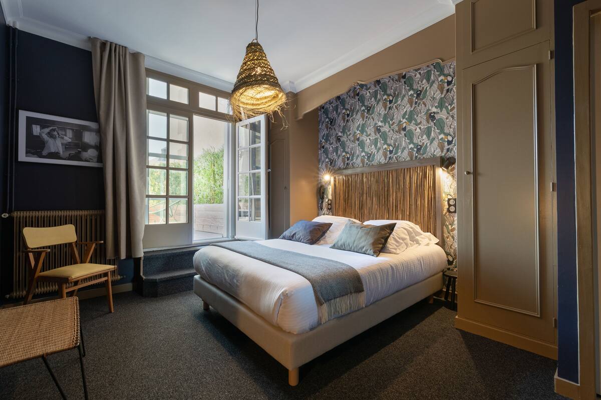 A bedroom with a large bed, a hanging light fixture, a window with curtains, a radiator, and a framed picture on the wall.