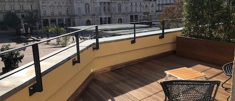 A wooden deck with a table and chairs, overlooking a cityscape with historic buildings.