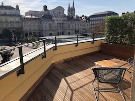 Terraza de madera con mesa y sillas, con vistas a un paisaje urbano con edificios históricos.