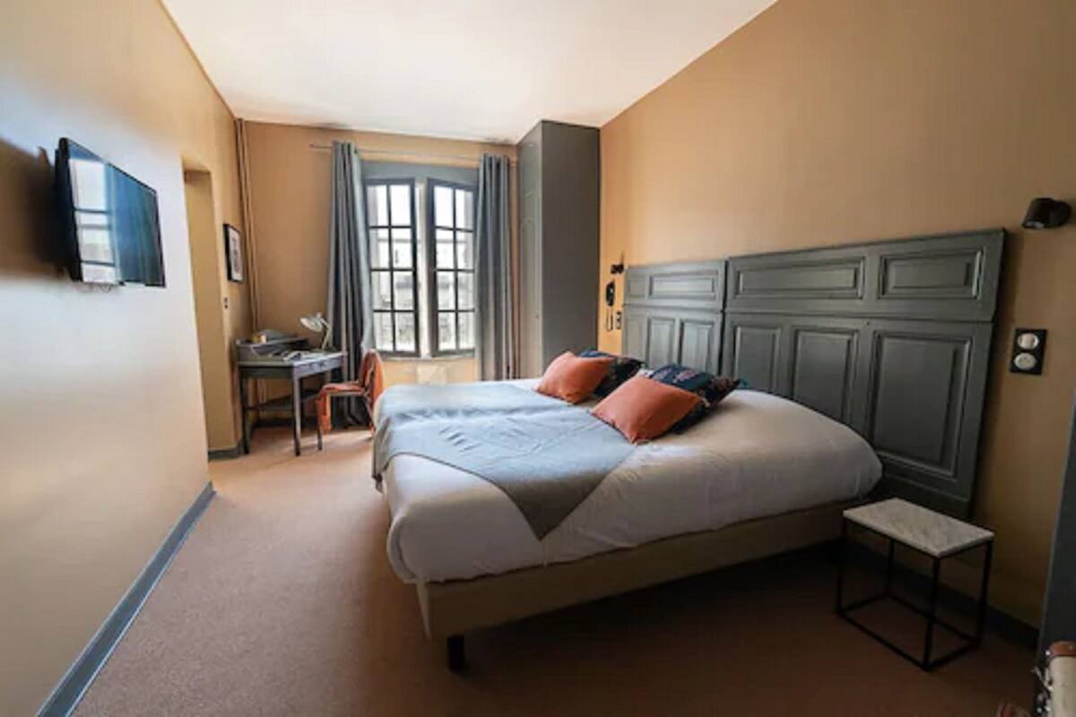 A bedroom with a bed, a desk, a chair, and a television on the wall.