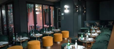 A restaurant with round tables, green chairs, and yellow ottomans.