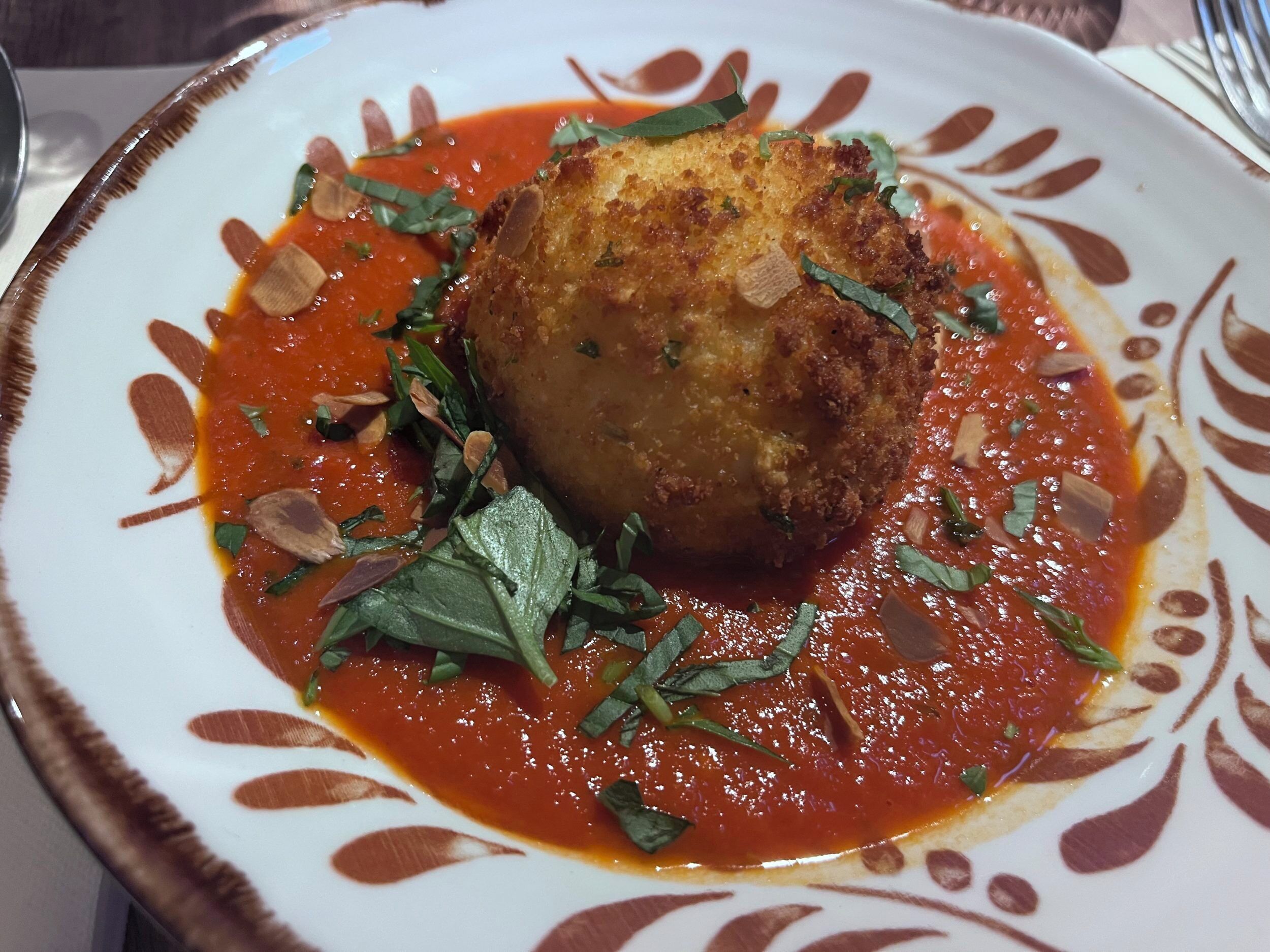 A plate with a breaded item and sauce, garnished with herbs.