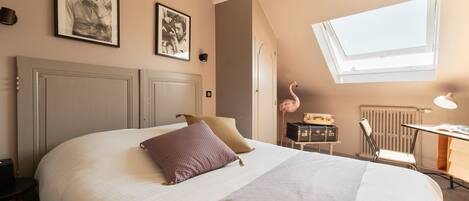 A bedroom with a large bed, a desk with a lamp, a radiator, and a skylight.