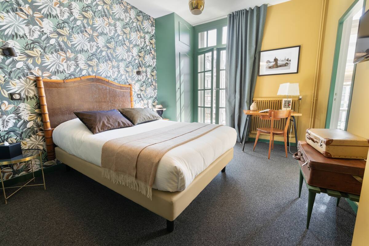 A neatly arranged hotel room with a bed, a chair, a table, and a window with curtains.