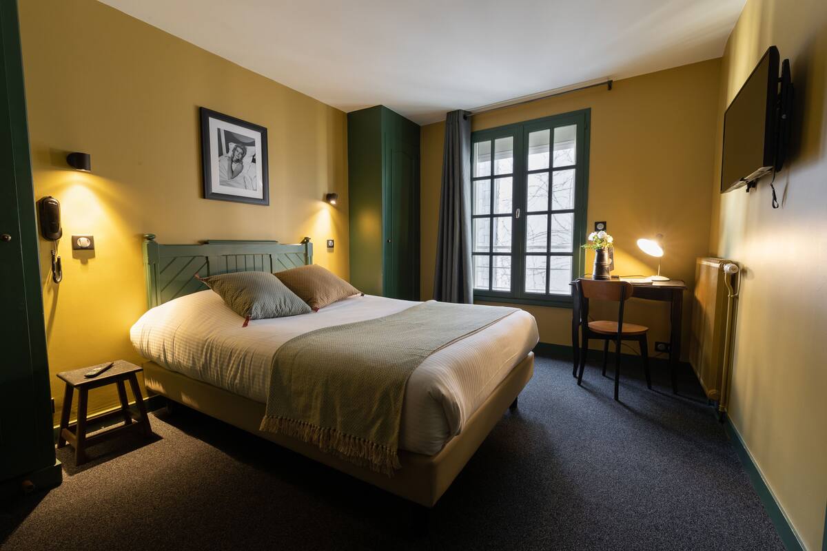 A hotel room with a bed, bedside table, lamp, and a window with curtains.