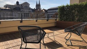 A rooftop terrace with two black mesh chairs and a wooden table, overlooking a historic building with spires. - Hôtel Saint Julien (Angers)