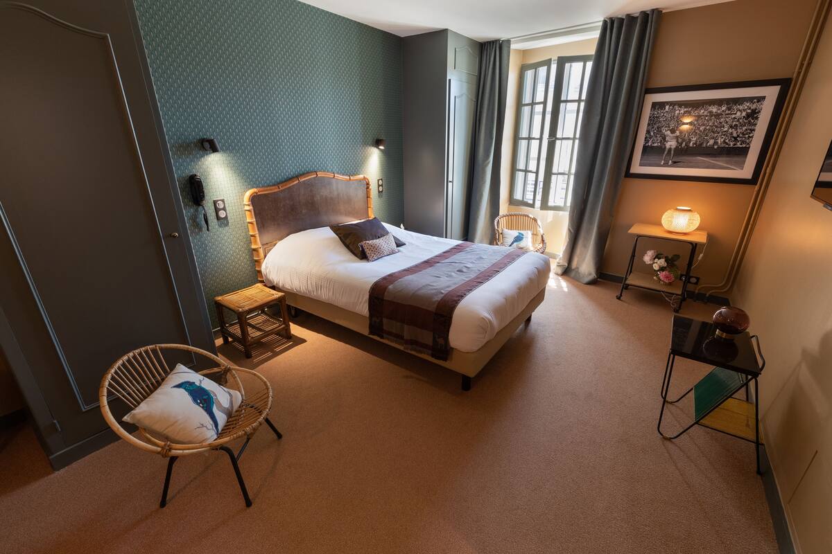 A neatly arranged bedroom with a bed, two chairs, a bedside table, and a wall-mounted lamp.