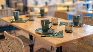 Un espace repas avec des tables préparées pour deux personnes, comprenant des chaises en osier et une table en bois.