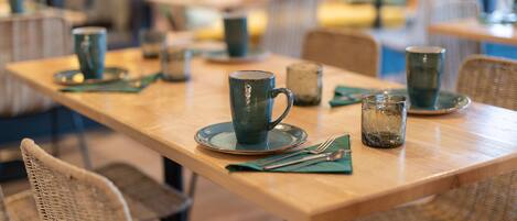 A dining area with tables set for two, featuring wicker chairs and a wooden table.