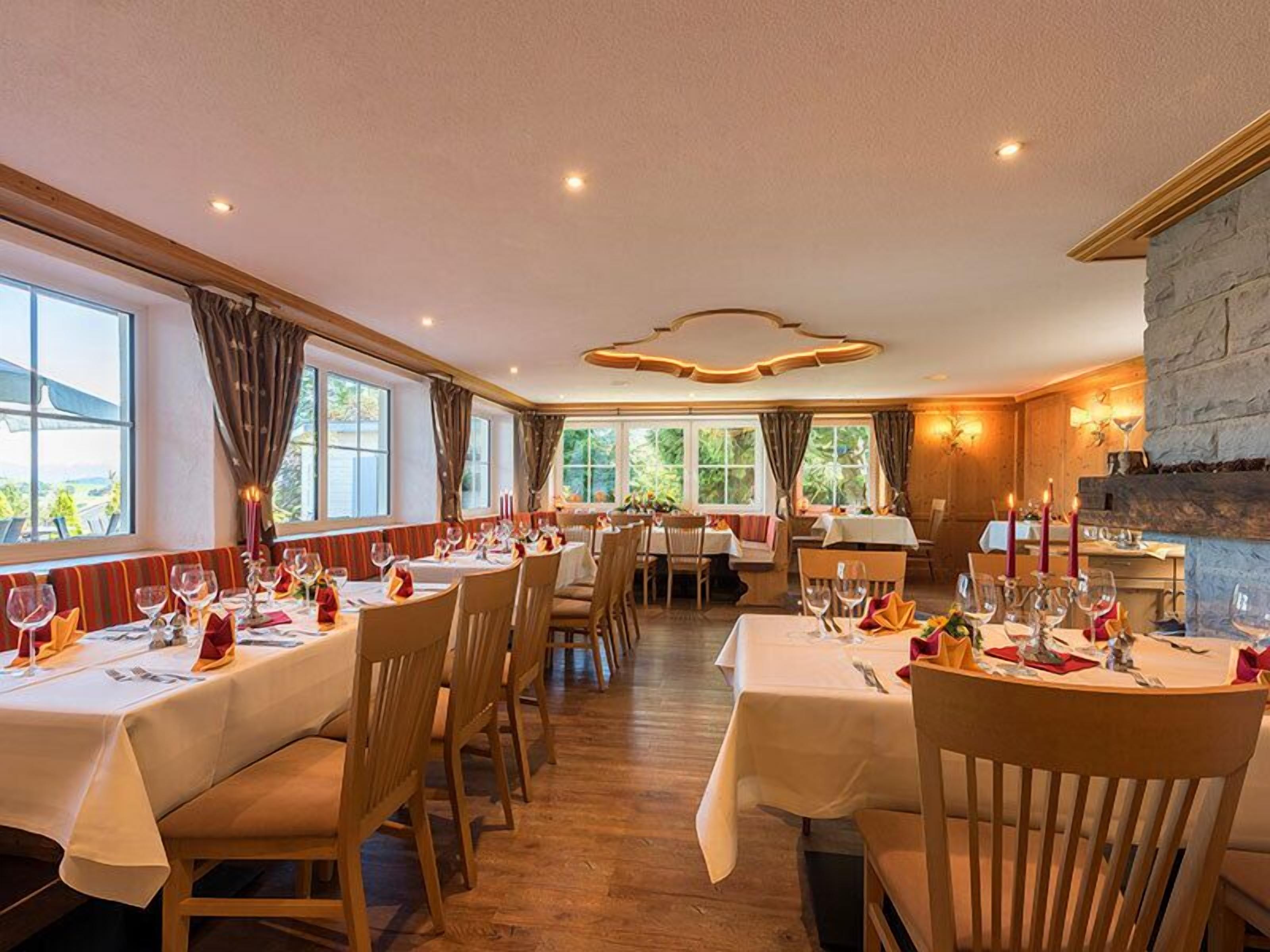 Un restaurant avec de nombreuses tables dressées pour le service, des chaises en bois et une cheminée en pierre.