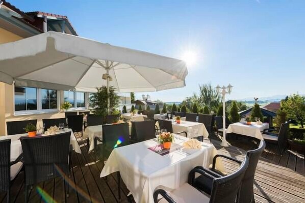 Un área de comedor al aire libre con mesas y sillas, protegida por sombrillas, con vistas a un paisaje.