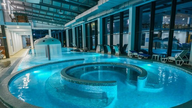 Ein innenliegender, kreisförmiger Pool, umgeben von Liegestühlen und einer Glaswand.