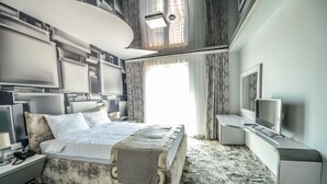 Ein modernes Hotelzimmer mit einem großen Bett, einem Fernseher, einem Schreibtisch und einem großen Fenster.