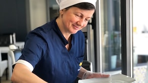 Eine Person in blauer Uniform und weißem Hut schneidet eine Torte auf einer Glasplatte.