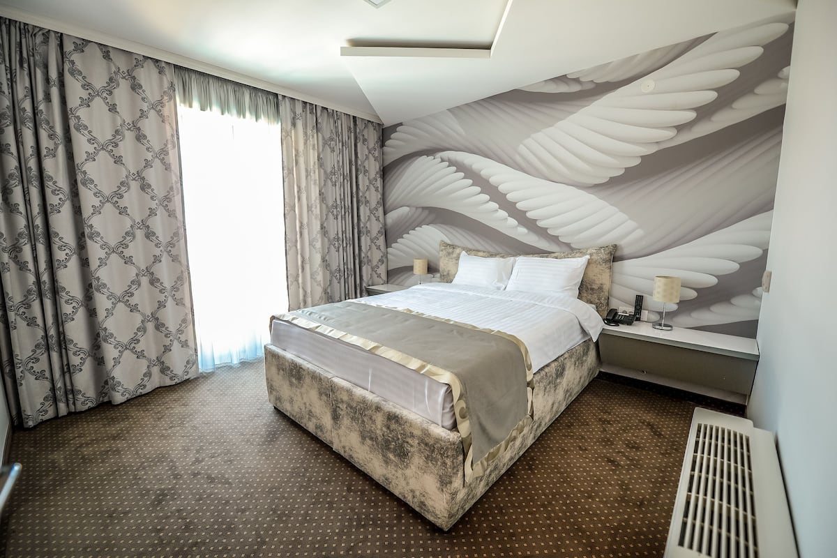 A hotel room with a large bed, a nightstand, a lamp, and a wall mural of wings.