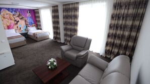 Ein Hotelzimmer mit Sofa, Sessel, zwei Betten, einem kleinen Tisch mit Blumen und einem Wandgemälde.