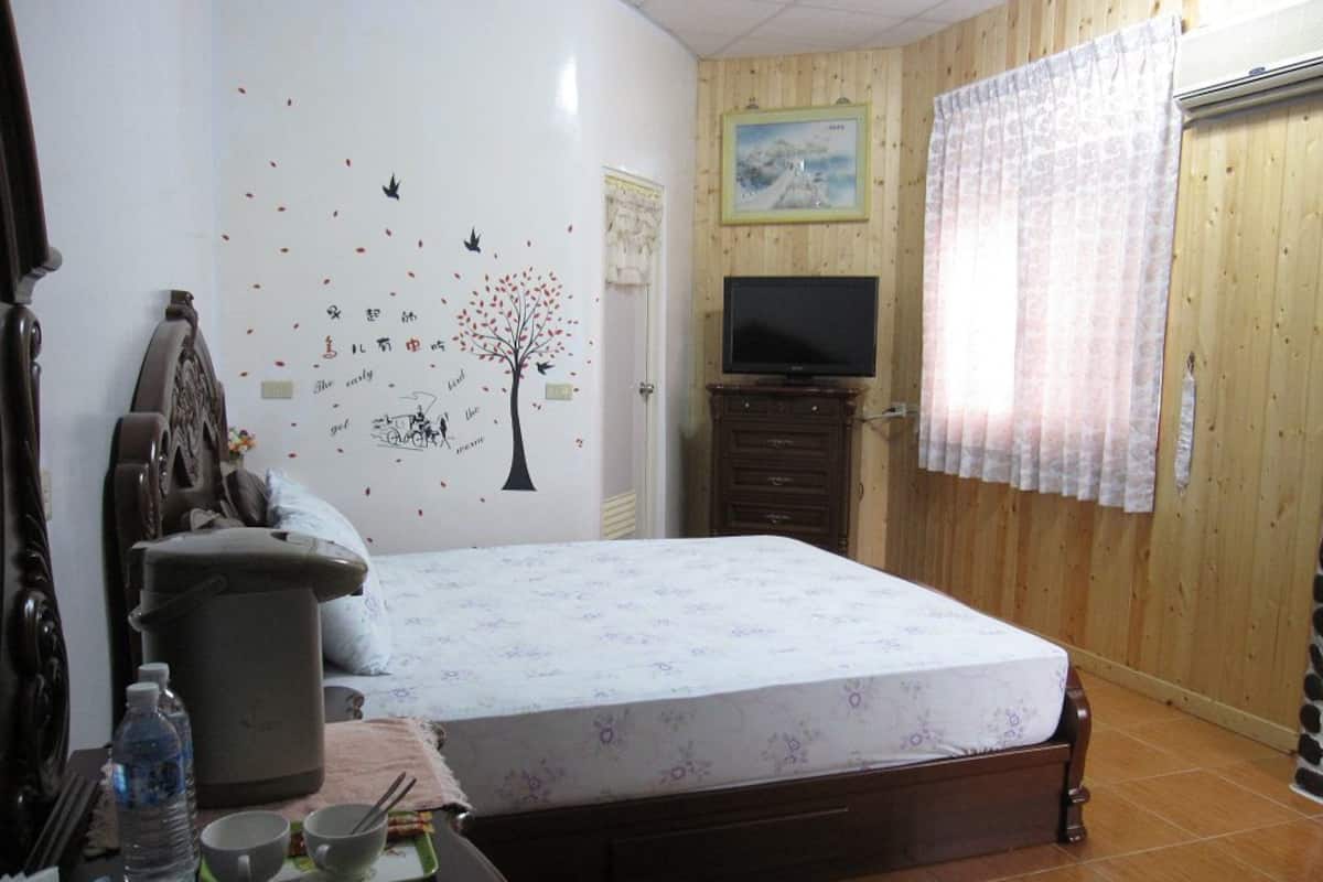 Un dormitorio con cama, televisor, armario de madera, ventana con cortinas y un vinilo decorativo en la pared.