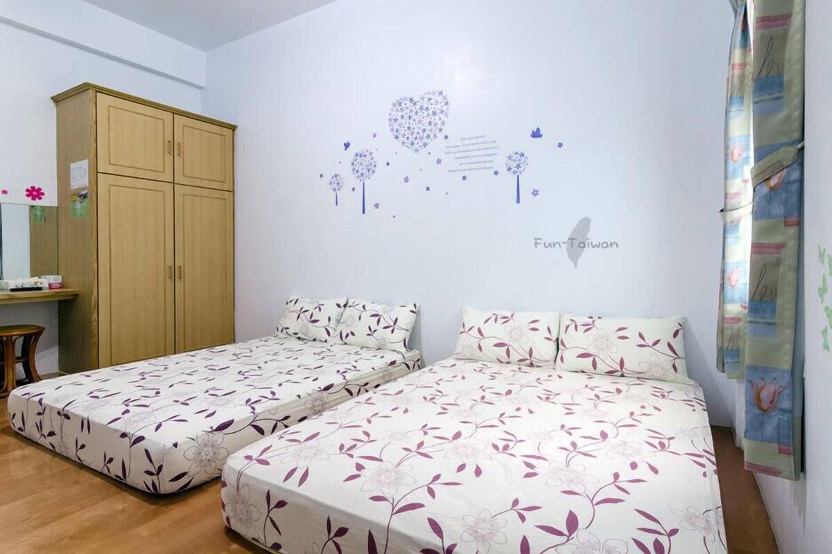 Un dormitorio con dos camas individuales, un armario de madera y una pared decorada con un diseño de corazón y el texto "Fun-Taiwan".
