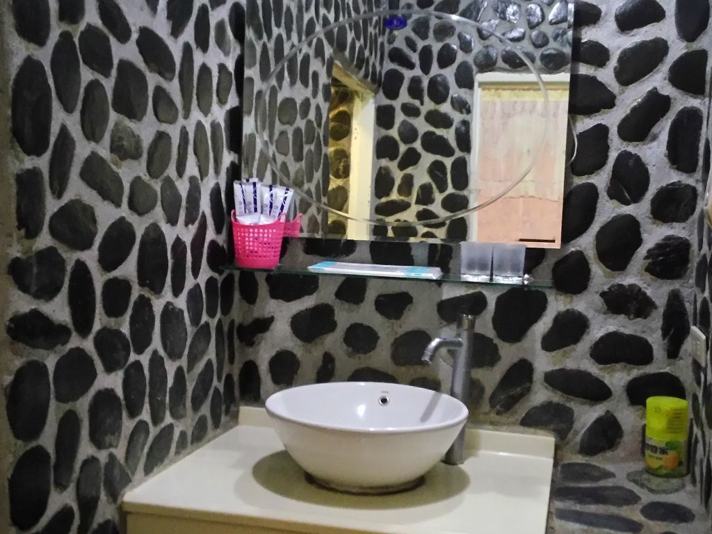 Un bany amb una paret amb relleu de pedra, un lavabo blanc, un mirall i una estant amb productes de tocador.