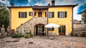 A yellow building with a stone staircase, a door, and a stone patio with an umbrella. - Cappannelle Country House Tuscany (Castiglion Fibocchi)
