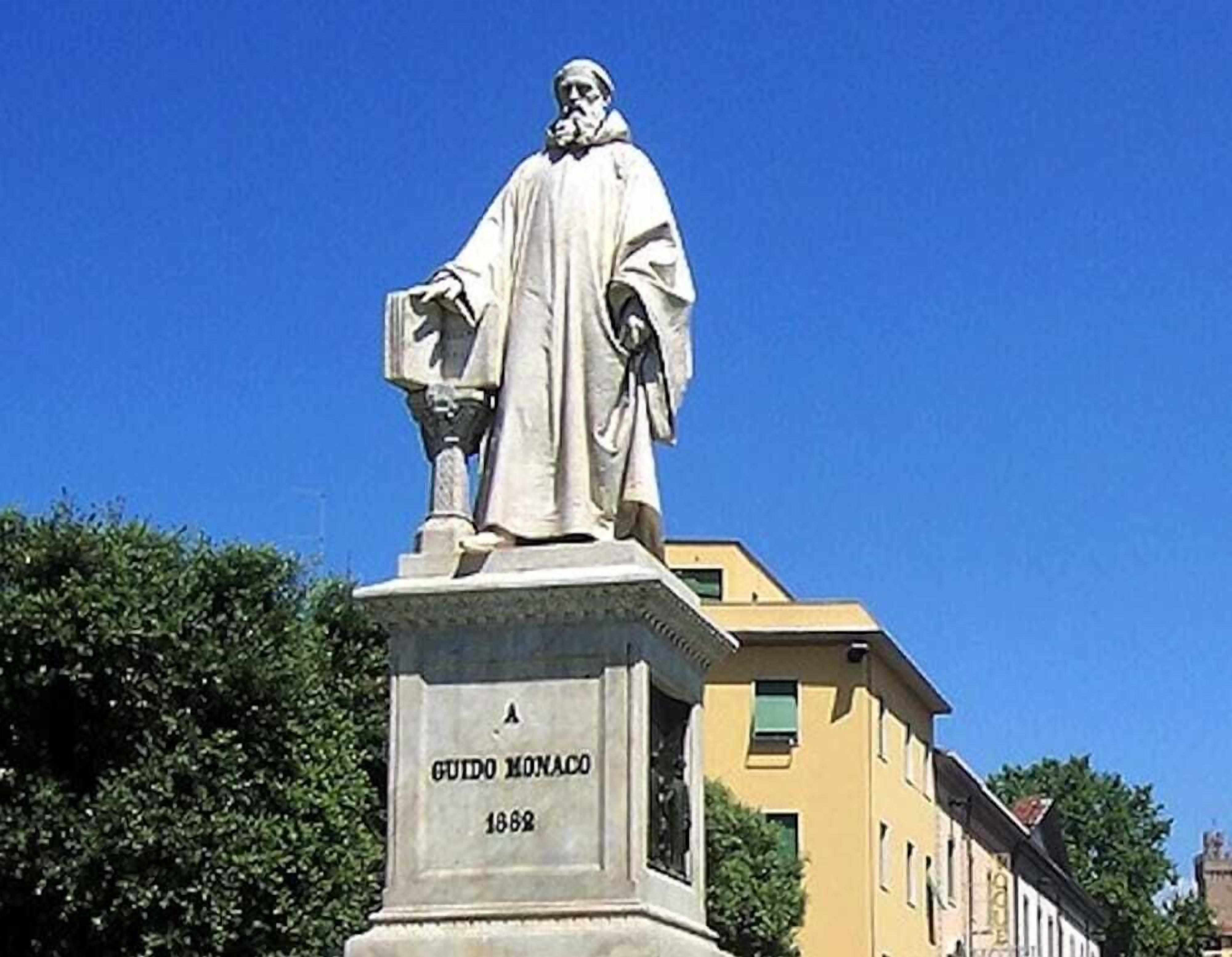 Eine Statue eines Mannes in einer Robe mit einem Sockel, auf dem 'GUIDO MONACO 1882' steht.