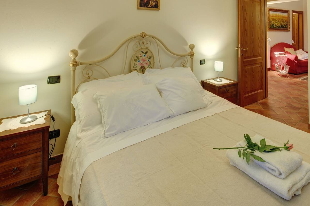 Een net opgemaakt bed met witte lakens, een nachtkastje met een lamp en een telefoon.