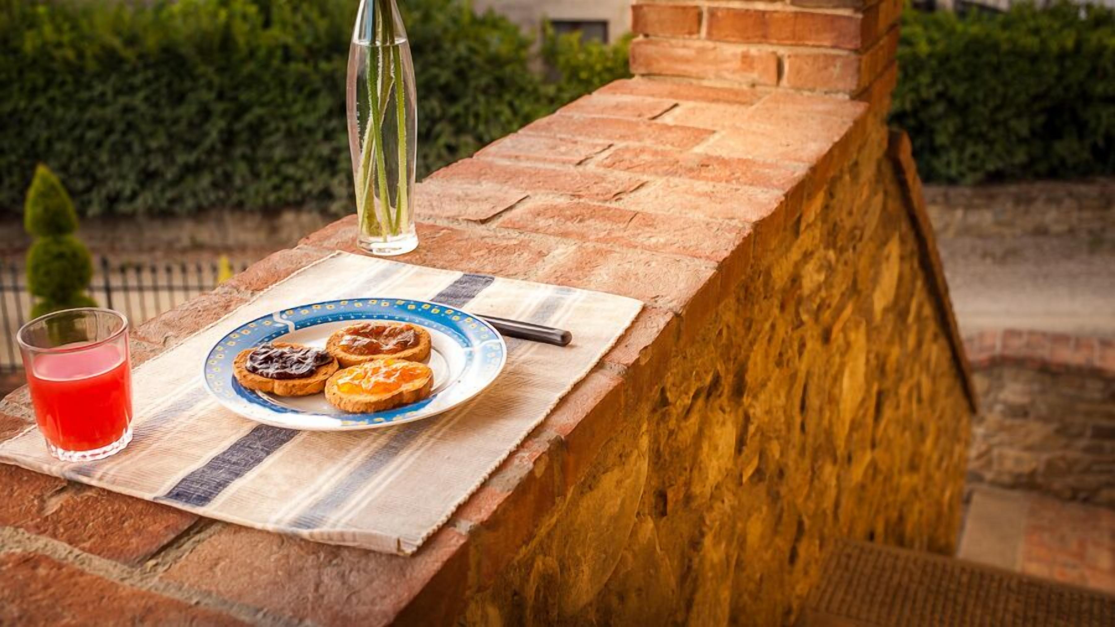 A breakfast setting with toast, jam, and a glass of red drink on a brick ledge.
