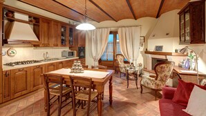 A cozy kitchen with wooden cabinets, a dining table with chairs, and a fireplace. - Cappannelle Country House Tuscany (Castiglion Fibocchi)