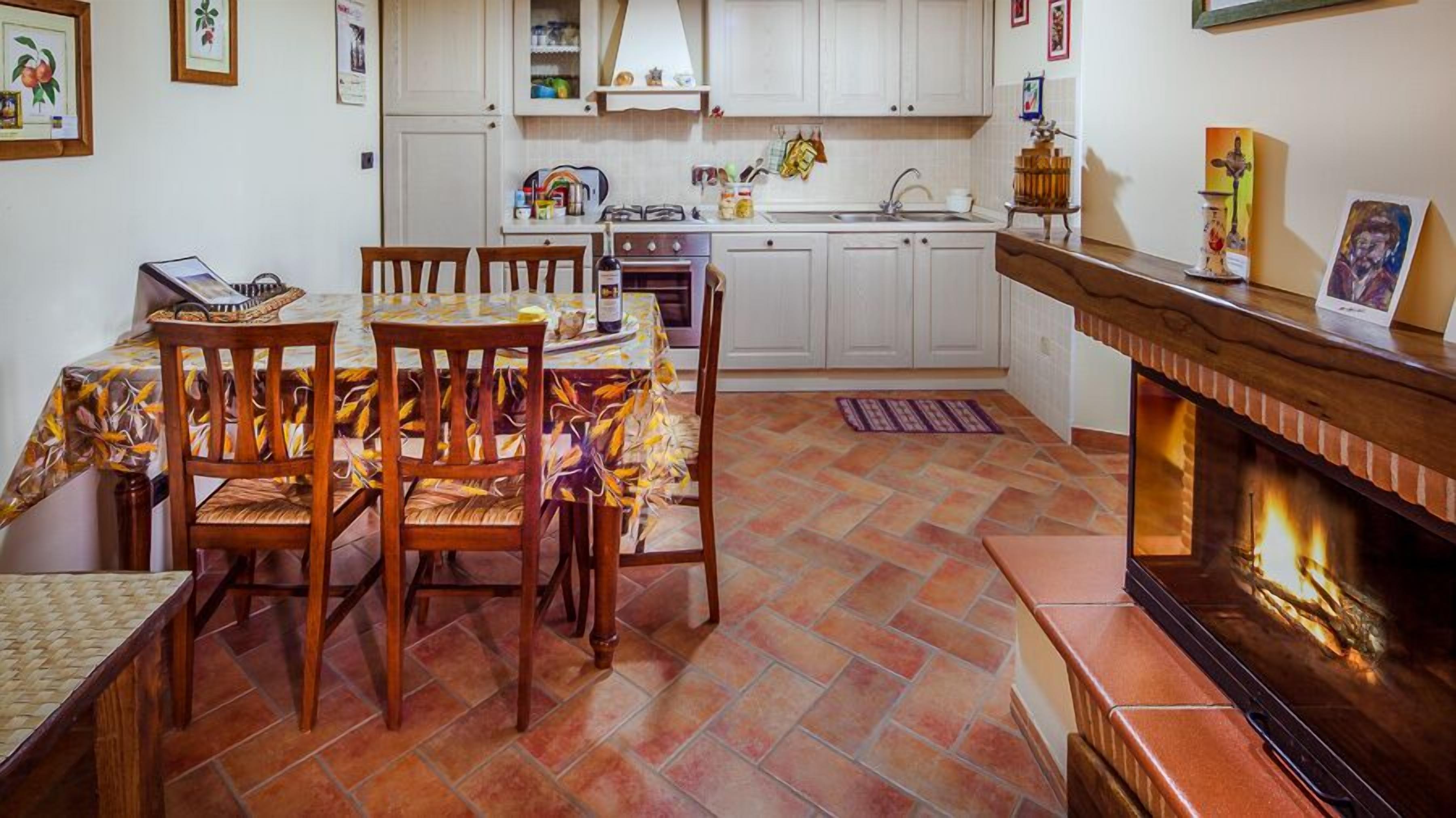 Un salon chaleureux avec une cheminée, un coin repas avec des chaises en bois et une table, et une cuisine avec des meubles blancs et un dosseret carrelé.