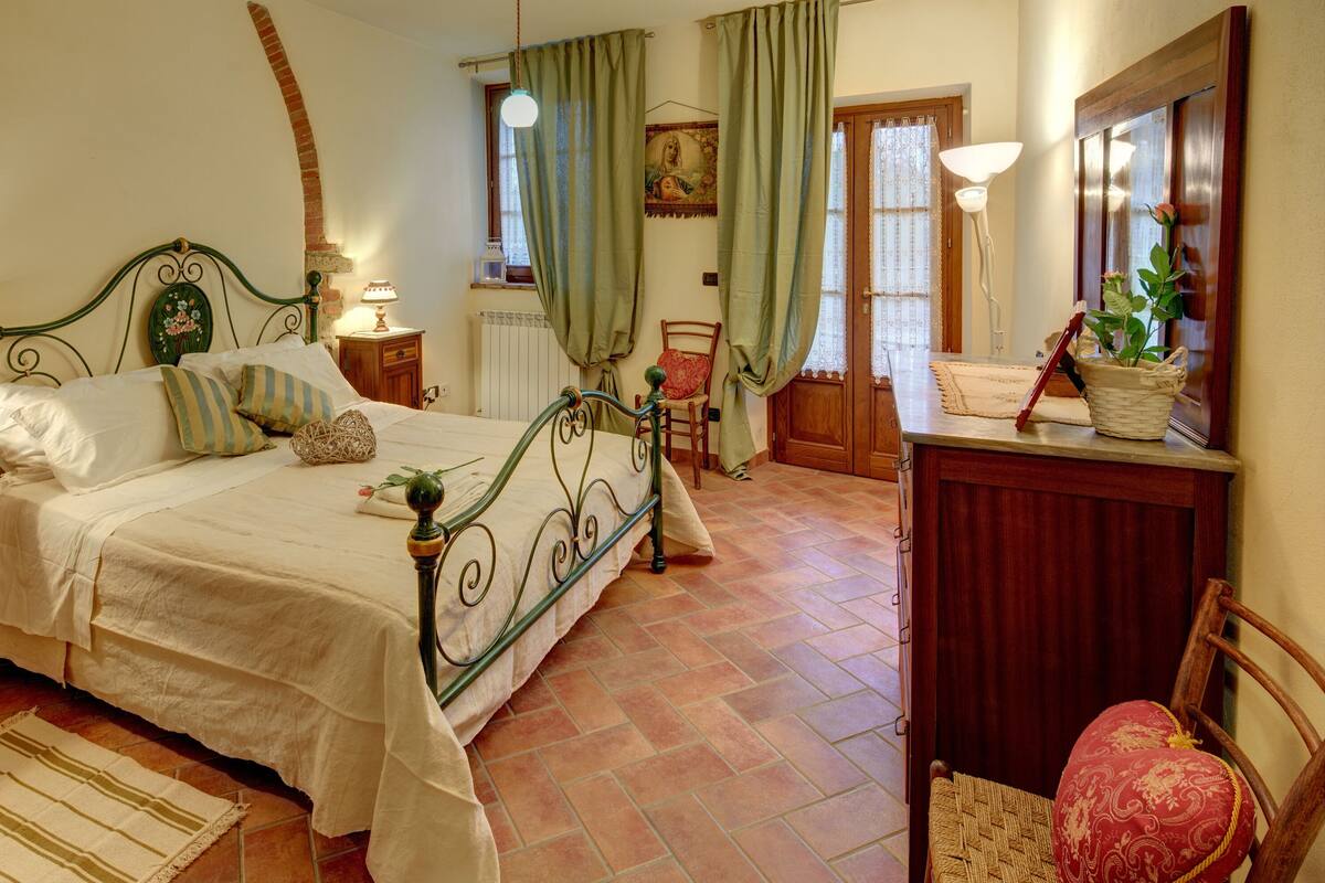 Een slaapkamer met een bed, nachtkastjes, een dressoir, een stoel en een potplant.