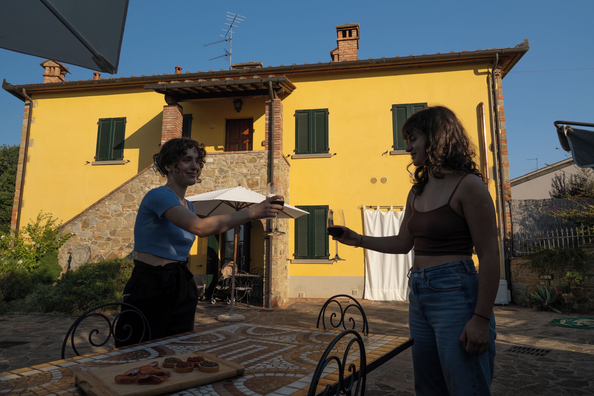 Un edificio giallo con dettagli in pietra, un patio piastrellato e un tavolo imbandito.