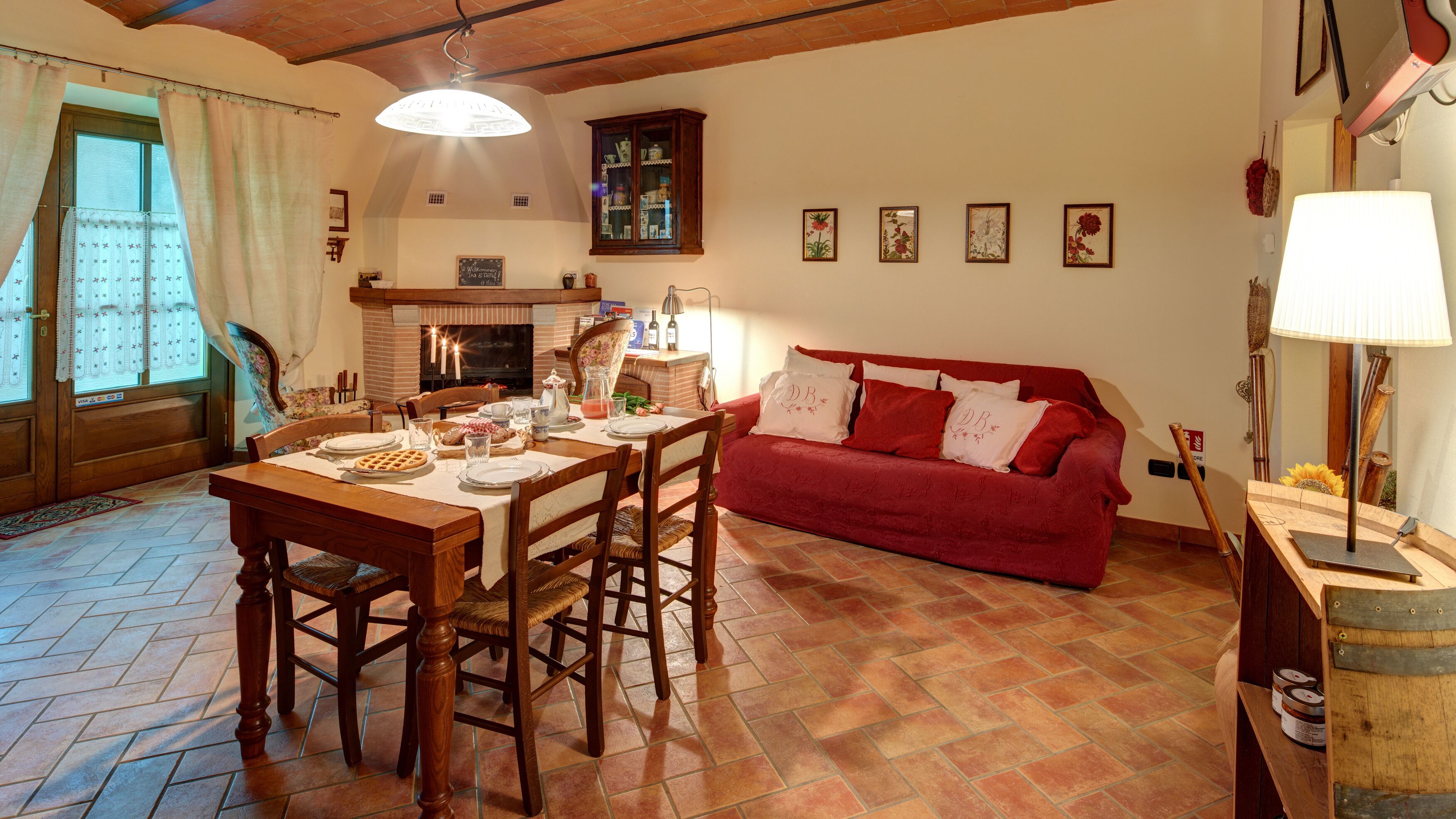 A cozy living room with a fireplace, a dining table set for a meal, and a red sofa.