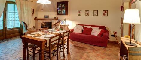 A cozy living room with a fireplace, a dining table set for a meal, and a red sofa.