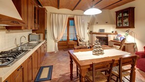 A cozy kitchen with wooden cabinets, a gas stove, a microwave, and a dining area with a table and chairs. - Cappannelle Country House Tuscany (Castiglion Fibocchi)