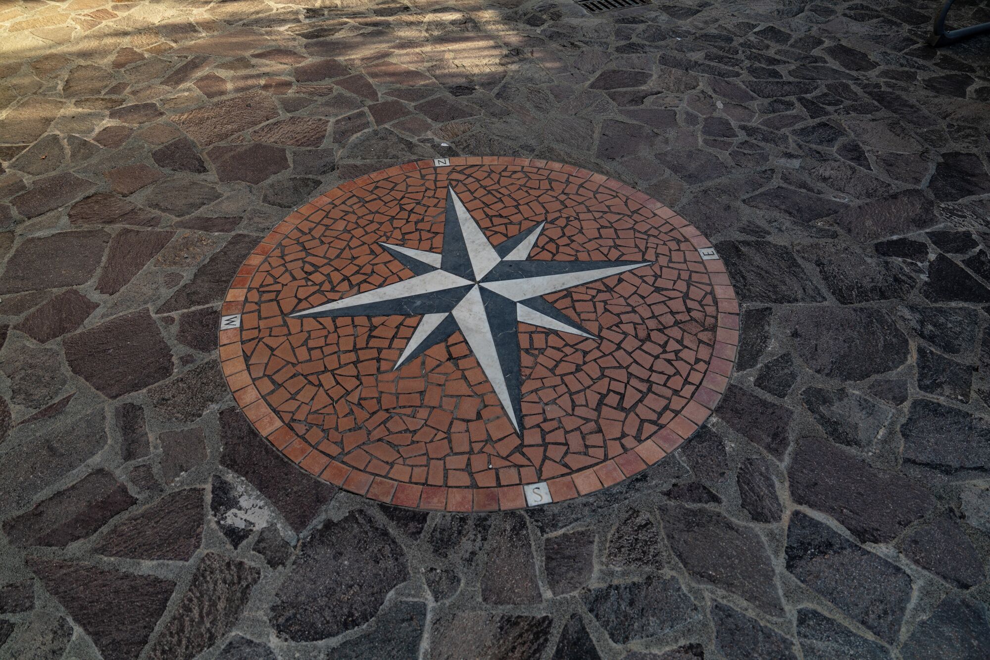 Une mosaïque circulaire représentant une boussole, incrustée dans un pavage de pierre.
