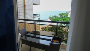 Ein Balkon mit Glastisch und Stühlen, der Blick auf das Meer und ein Gebäude mit Ziegeldeckung bietet.