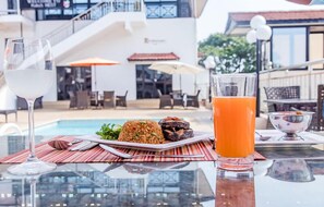 A dining table with a plate of food, a glass of white wine, and a glass of orange juice. - Hotel Barmoi (Freetown)