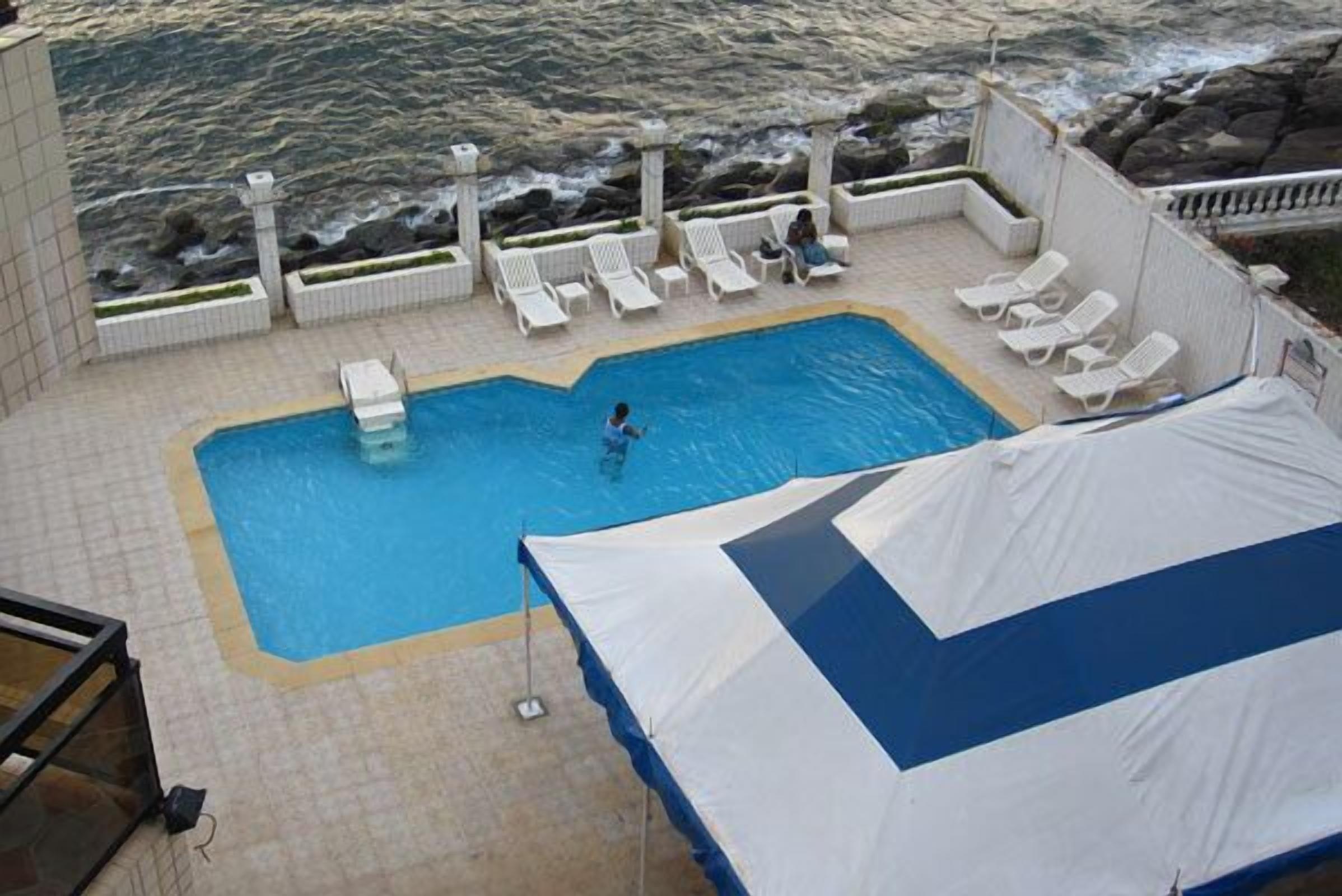 Un área de piscina con vista al océano, sillas de descanso y una carpa.