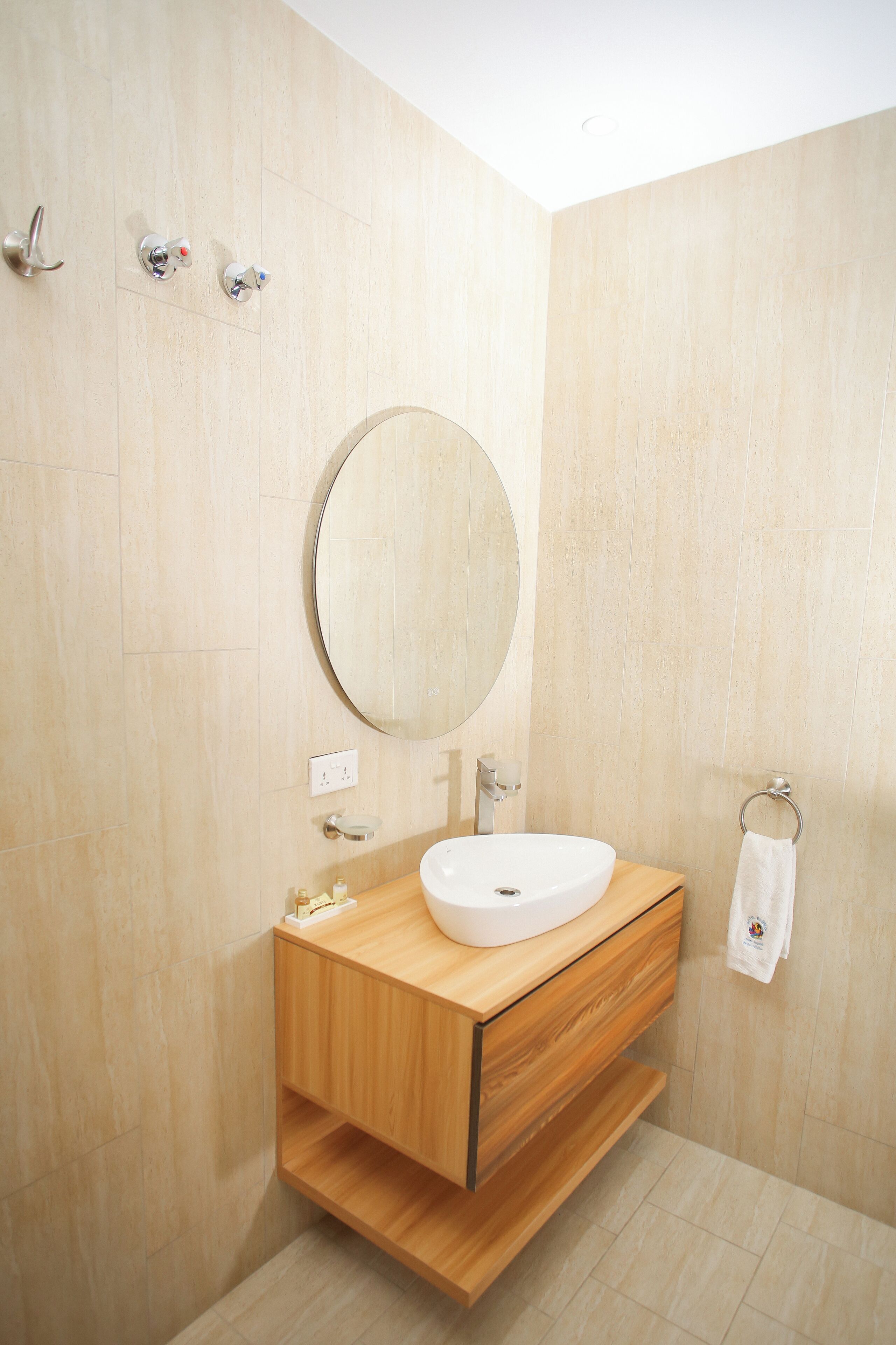 A modern bathroom with a wooden vanity, a round mirror, and a towel ring.