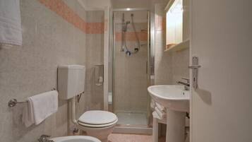 Un baño con inodoro, bidé y ducha con mampara de vidrio.