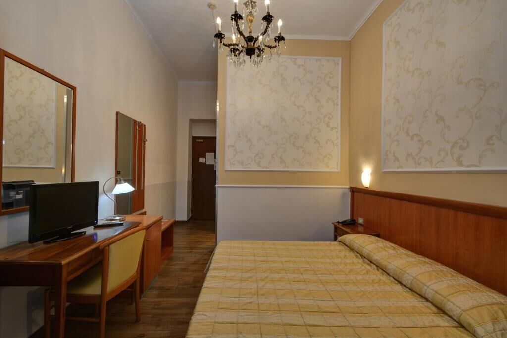 Une chambre d’hôtel comprenant un lit, un bureau avec un ordinateur, une chaise, une télévision et un lustre.